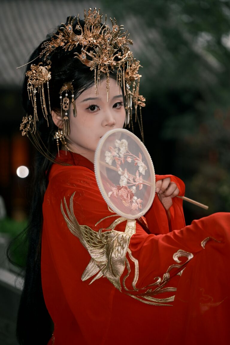 Asian woman in ornate traditional Hanfu with intricate headpiece and handheld fan.